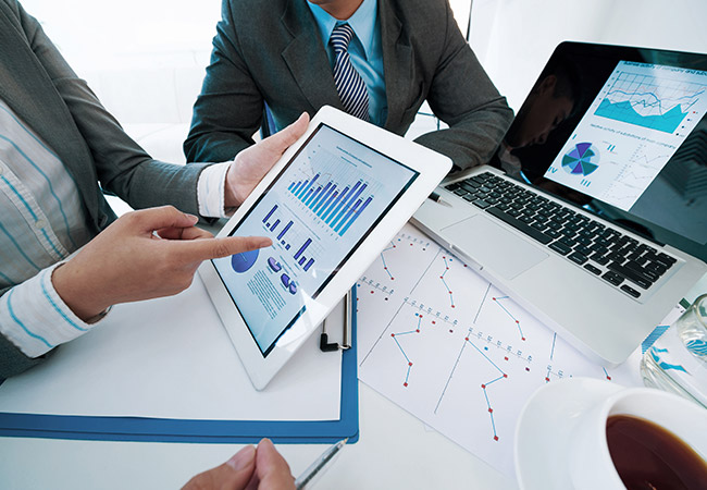 worker in a suit showing their colleagues an ipad depicting various graphs