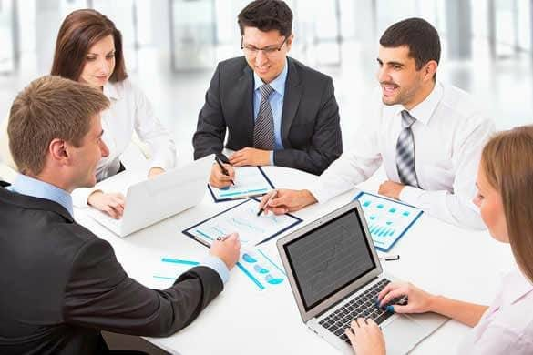 group of employees in suits working on organisational capability on their laptops with papers on the desk